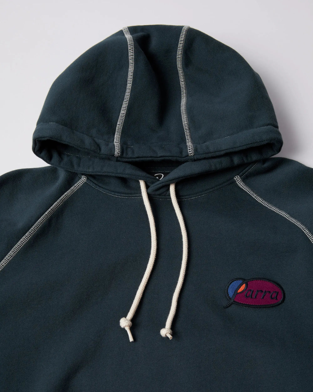 Detail of dark blue ByParra hooded sweatshirt with white contrast stitching and embroidered chest logo.